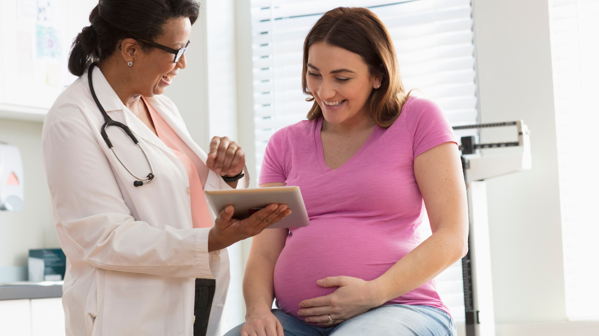 Pregnant woman in pink shirt with her female doctor smiling while looking a